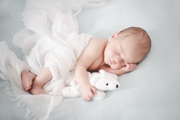 Ein Baby schläft und hält einen Teddybär unter dem Arm.