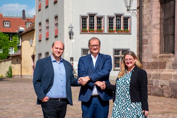 Vor dem Villinger Rathaus stehen die drei Personen zusammen. OB Roth gibt beiden über Kreuz die Hand.