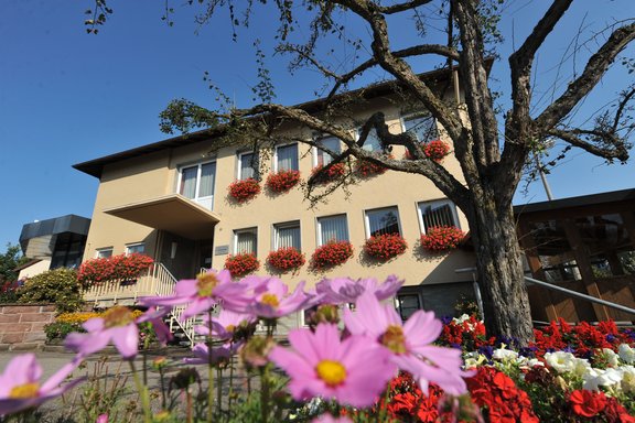 Gebäude der Ortsverwaltung Obereschach, davor lilane Blumen