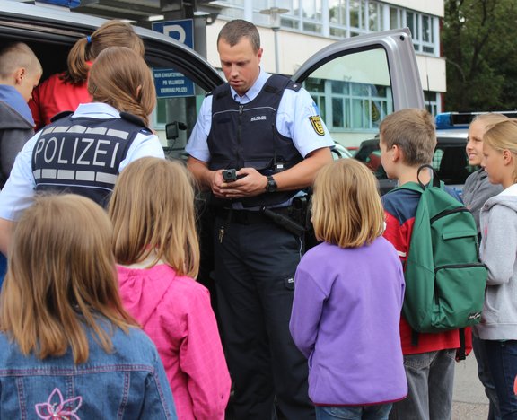 Zwei Polizisten zeigen einer Gruppe von Kinder das Polizeiauto.