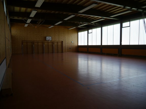 Spielfeld einer Turnhalle mit Basketballkörben und einer Sprossenwand