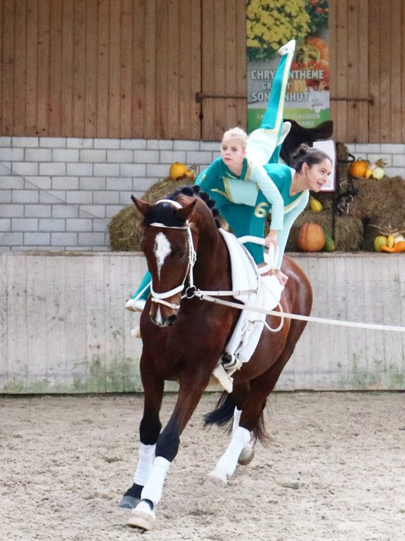 zwei Akkrobatinnen turnend und reitend auf einem Pferd