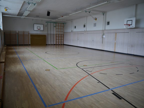 Turnhalle mit Parkettboden, mehreren Basketballkörben und Sprossenwänden an der Wand