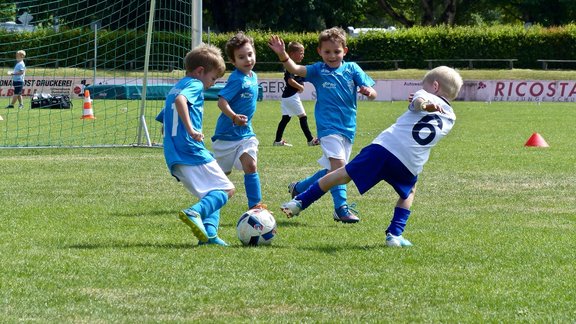 zwei Kinderfußballmannschaften, welche gegeneinander spielen. Wobei die eine Mannschaft probiert einen Schuss zu blocken.