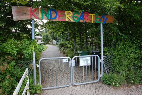 Eingangsbereich mit Gartentoren der Kindertagesstätte Pfaffenweiler und Holzschild mit bunten Buchstaben.