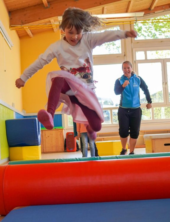 Ein Kind springt im vollen Lauf über ein kleines Hinderniss im Sportunterricht