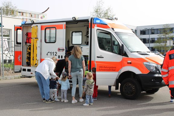 Der Krankenwagen hat die Tür geöffnet und die Kinder stehen davor und schauen in den Rettungswagen hinein.