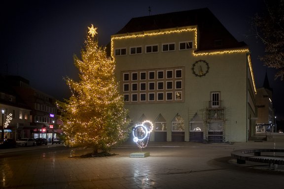 ein grünes Gebäude mit Lichterkette entlang des Dachabschlusses sowie ein Tannenbaum mit Lichterkette