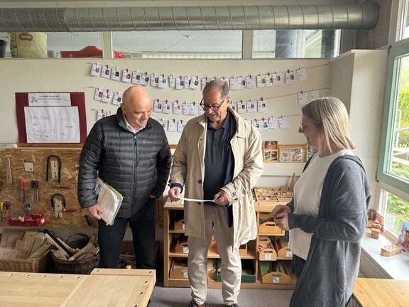 Jürgen Roth, Dieter Kleinhans und Cornelia Fuchs stehen in der Kita Ziegelbach. Gemeinsam betrachten sie Papiere der Projektplanung.