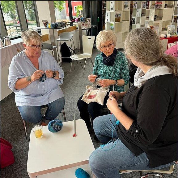 Drei Frauen sitzen im Halbkreis zusammen und stricken gemeinsam.