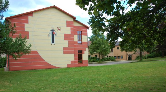 Gebäude, in dem sich die Grundschule befindet. Davor eine Wiese und Bäume.