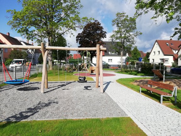 Auf dem Spielplatz sieht man die große Schaukel, die umgeben ist mit Rasen und schönen Wegen.