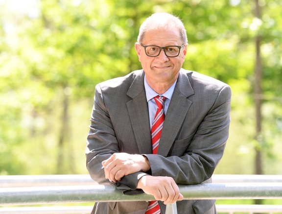 Oberbürgermeister Jürgen Roth lehnt in einem Park an einem Geländer und lächelt.