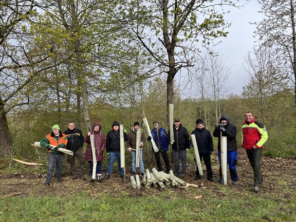 Die Gruppe der Stiftung Liebenau steht im Wald und hält die Baumschutzhüllen in den Händen.