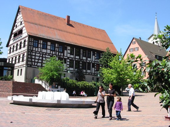 im Vordergrund ist ein Brunnen zu sehen. Im hintergrund ein altes Fachwerkhaus