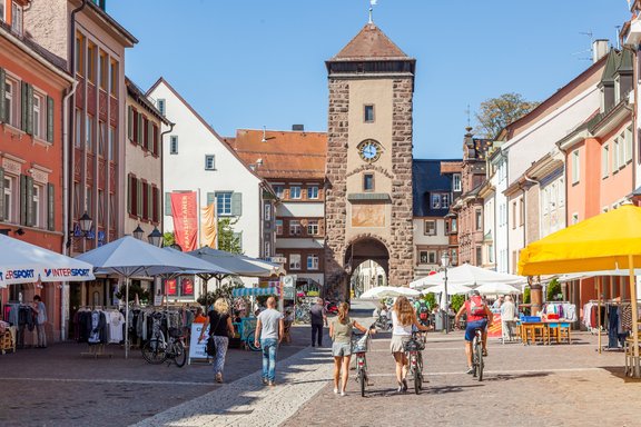 das Riettor. Im Vordergrund sind einige Menschen zu sehen, welche in der historischen Innenstadt einkaufen.