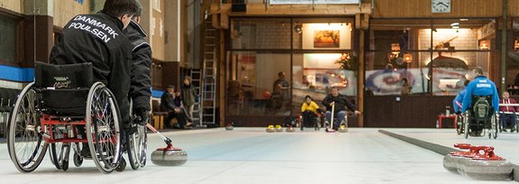 Ein Rollstuhl-Curler während er den Curlingstein spielt