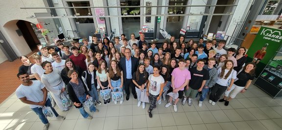 Die große Gruppe aus jungen Mädchen und Jungen steht gemeinsam mit OB Roth, der in der Mitte steht, eng zusammen im Foyer der Touristinfo.