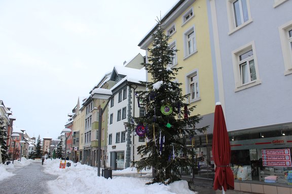 Bunt geschmückter Fasnetsbaum in der Villinger Rietstraße vor dem Geschäft Betten Gebers, im Hintergrund Blick auf das Bickentor mit Schnee auf der Straße.