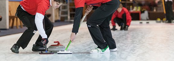 zwei Curler auf der Eisbahn schrubbend vor dem Curling-Stein