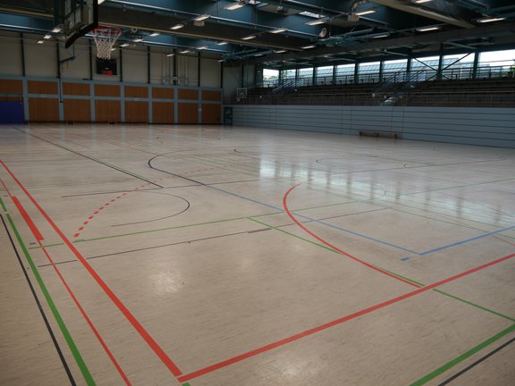 Innenansicht einer großen Sporthalle mit Spielfeld und Tribüne