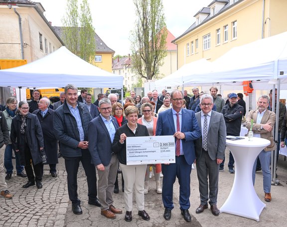 Bei einem Fest übergibt eine Frau, sie ist Ministerin, einen großen Scheck an OB Roth. Um sie herum stehen noch weitere Männer.